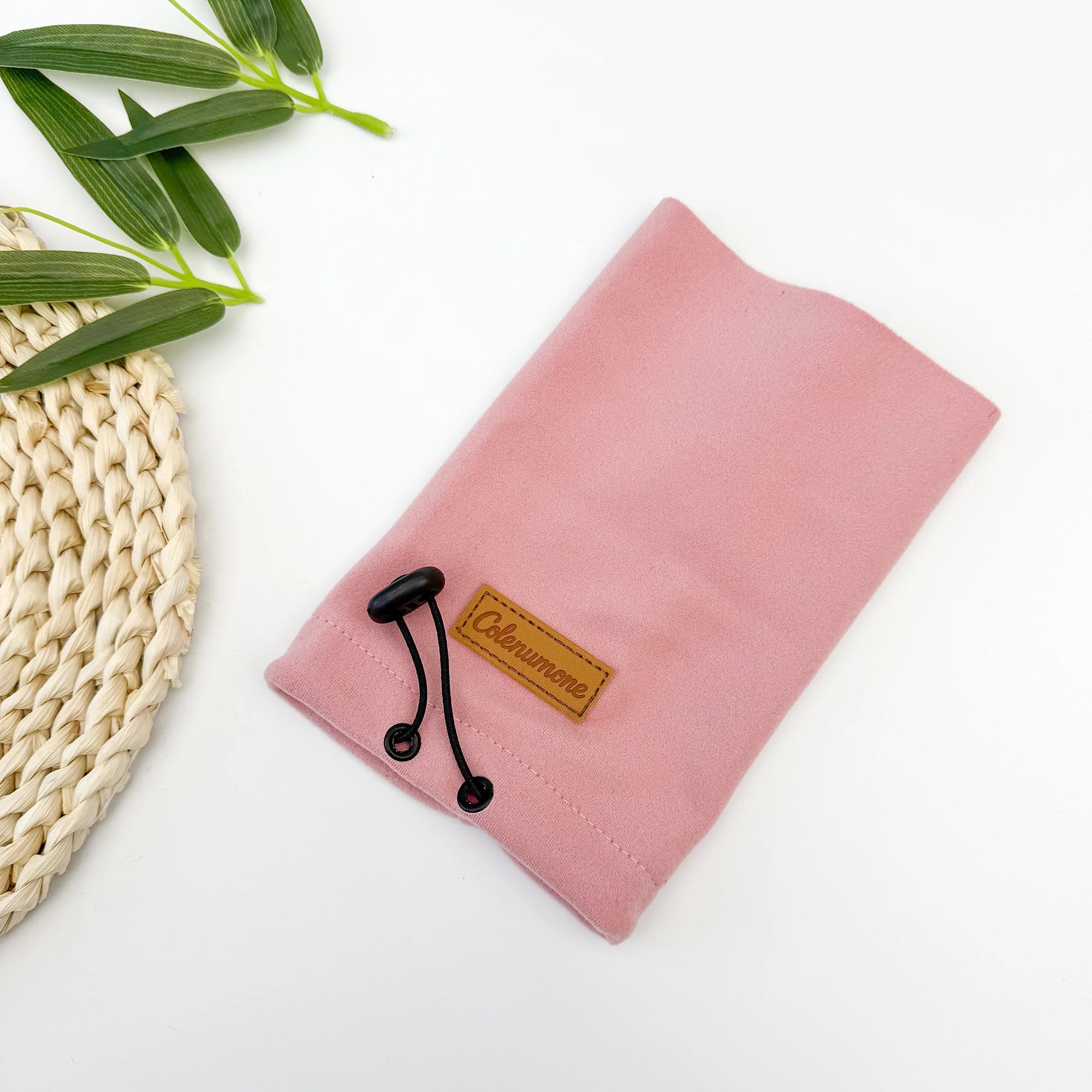 Pink fabric drawstring pouch with leather patch on white background, next to green leaves