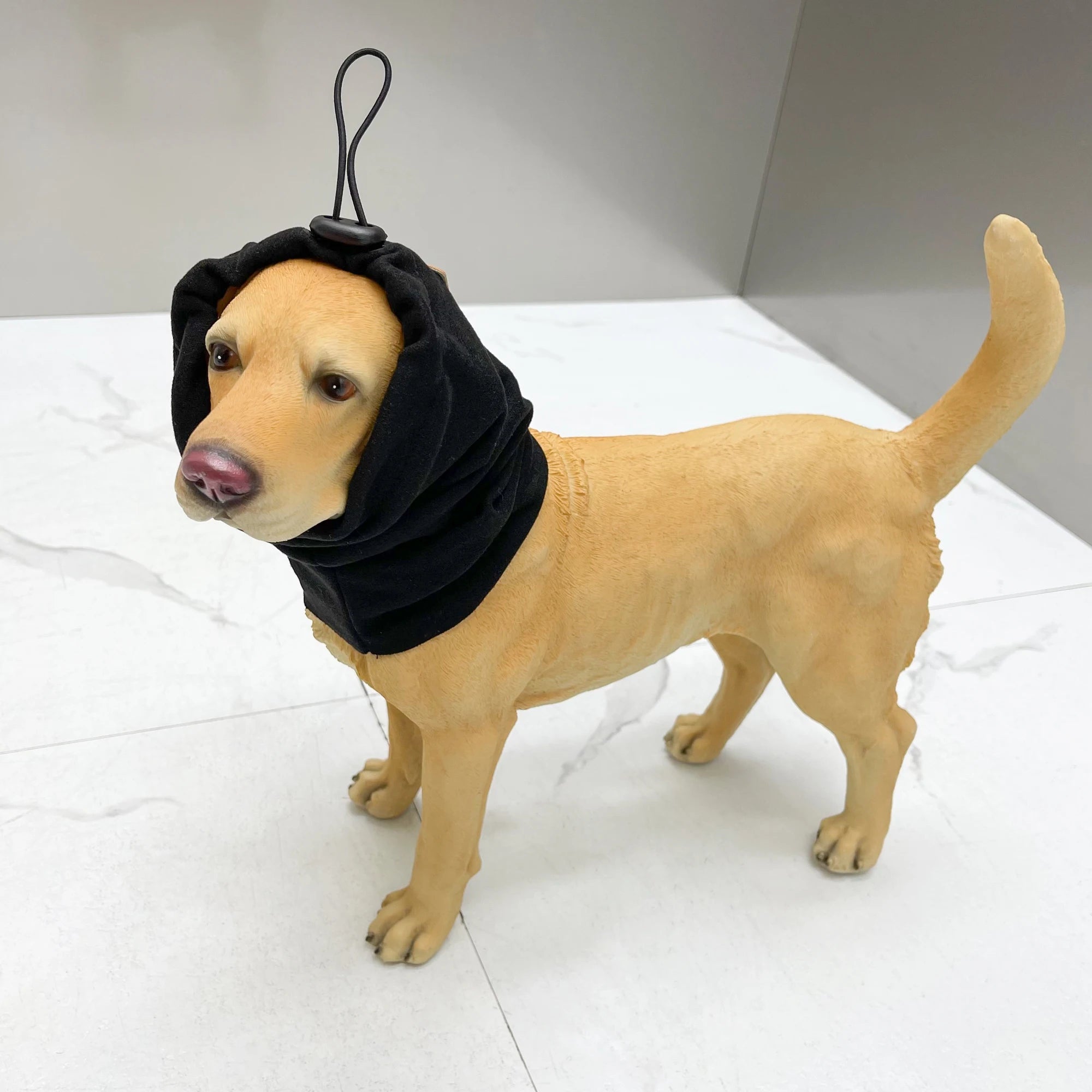 Yellow dog mannequin wearing black adjustable dog ear cover on white tile floor
