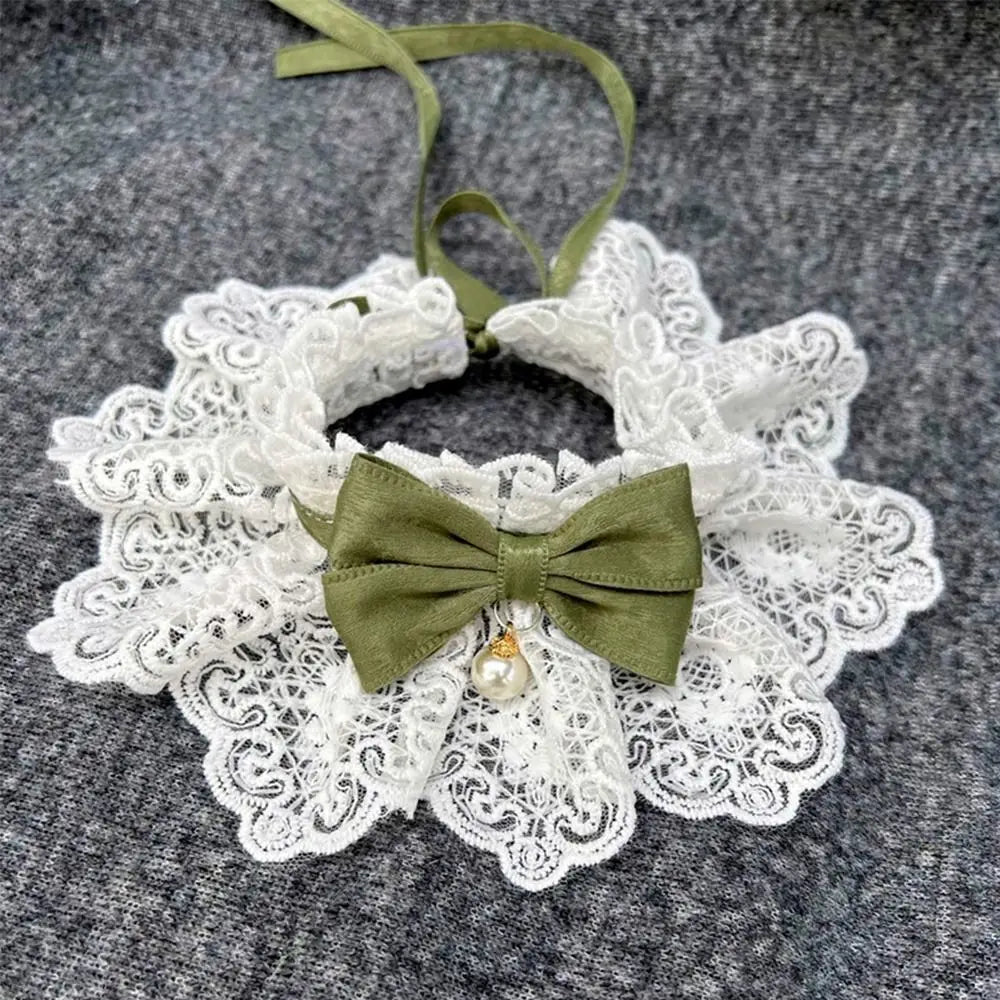 White lace dog collar with green bow and pearl charm on dark fabric background