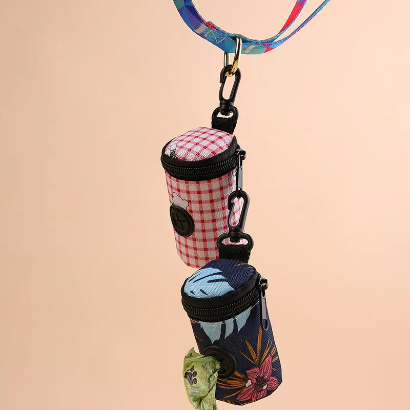 Two portable dog waste bag dispensers with floral and checkered designs hanging on a leash.