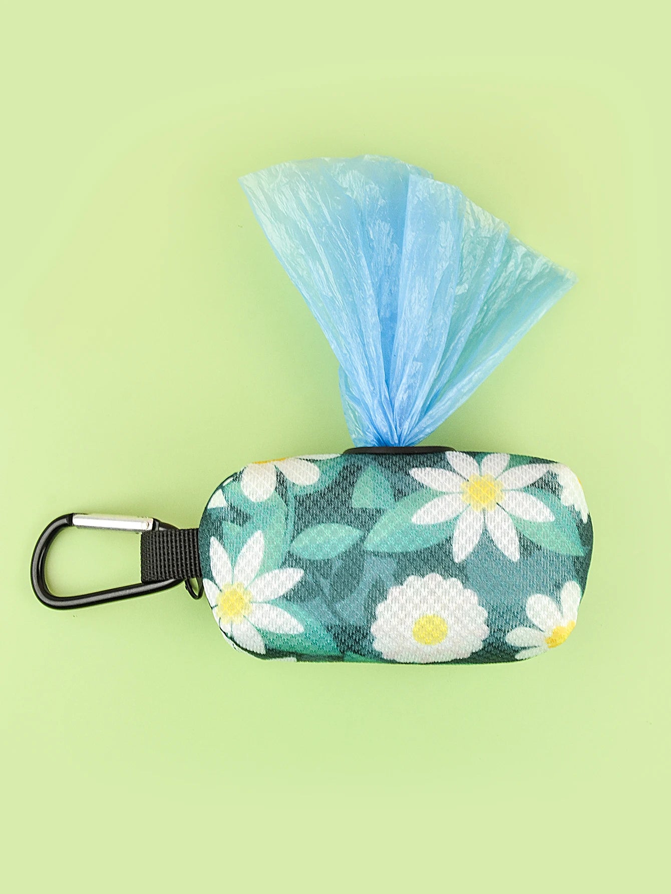 Floral dog poop bag holder dispenser with carabiner clip and blue bags on green background