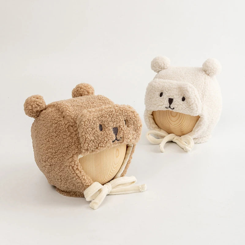 Two plush bear face dog hats with ear details, in beige and cream, displayed on wooden forms.