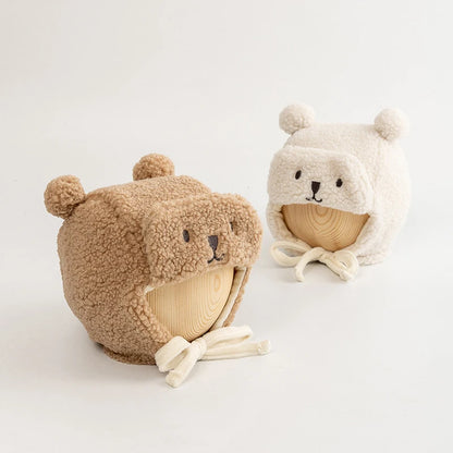 Two plush bear face dog hats with ear details, in beige and cream, displayed on wooden forms.