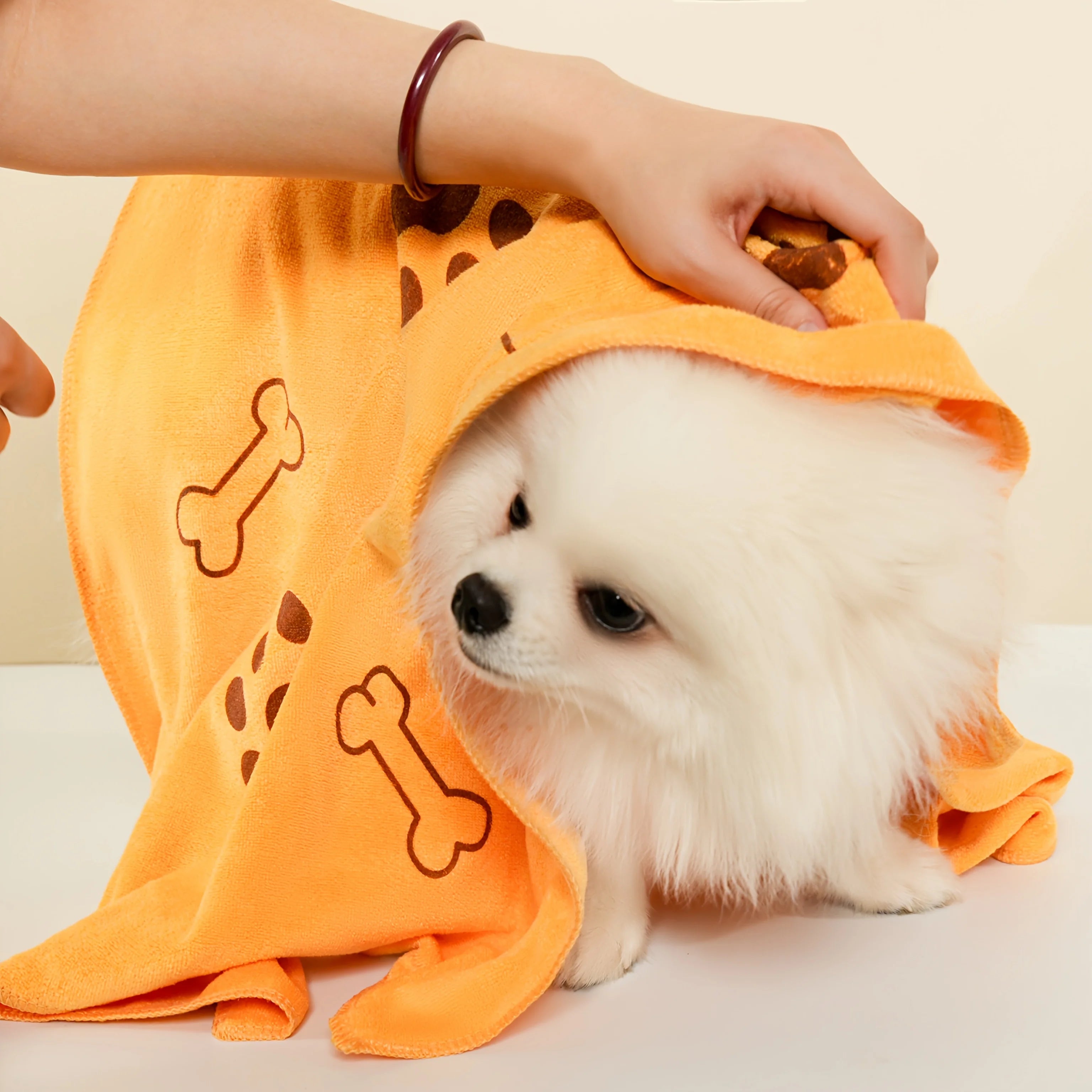 Fluffy white dog wrapped in orange dog towel with bone pattern, grooming accessory