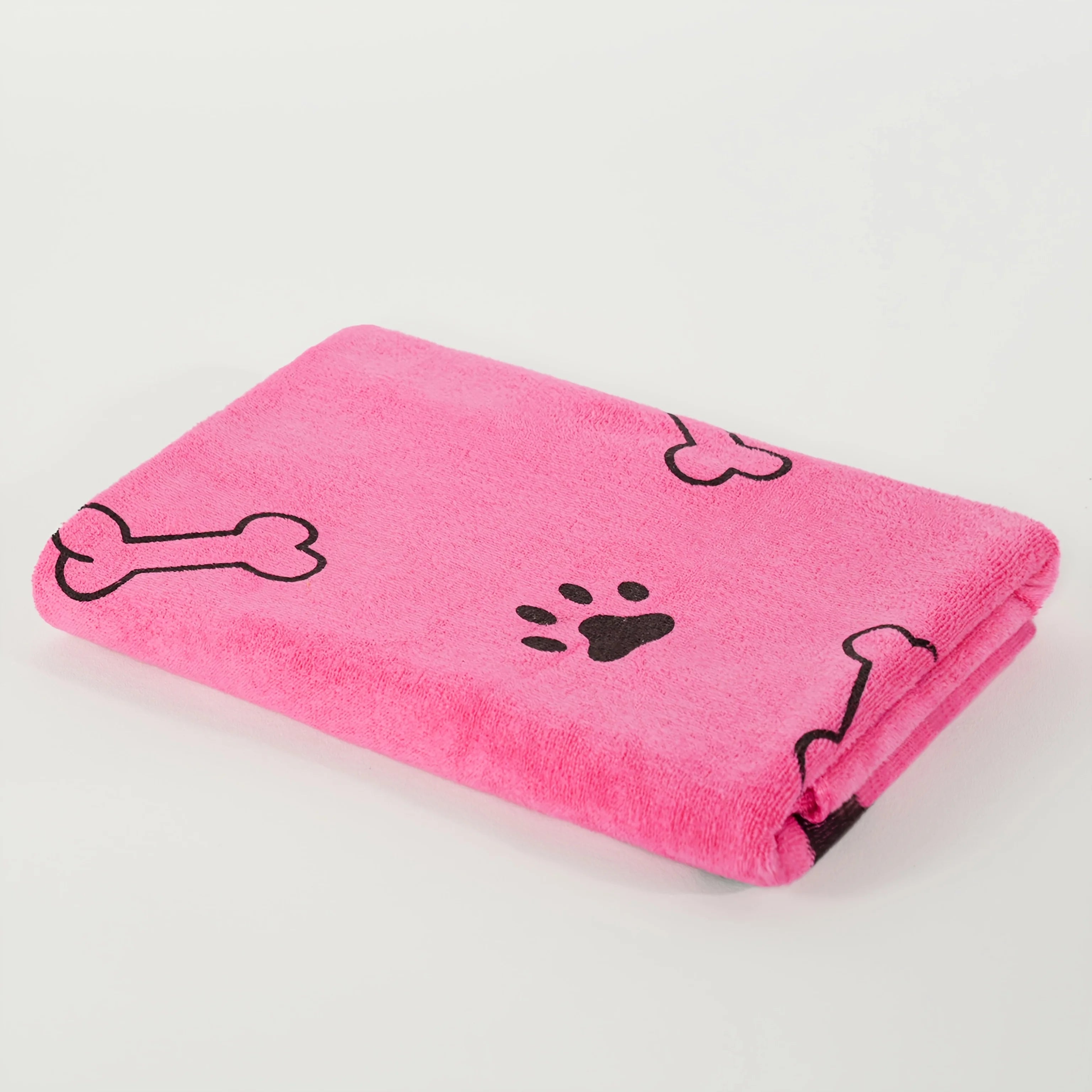 Folded pink dog towel with black paw print and bone pattern on white background