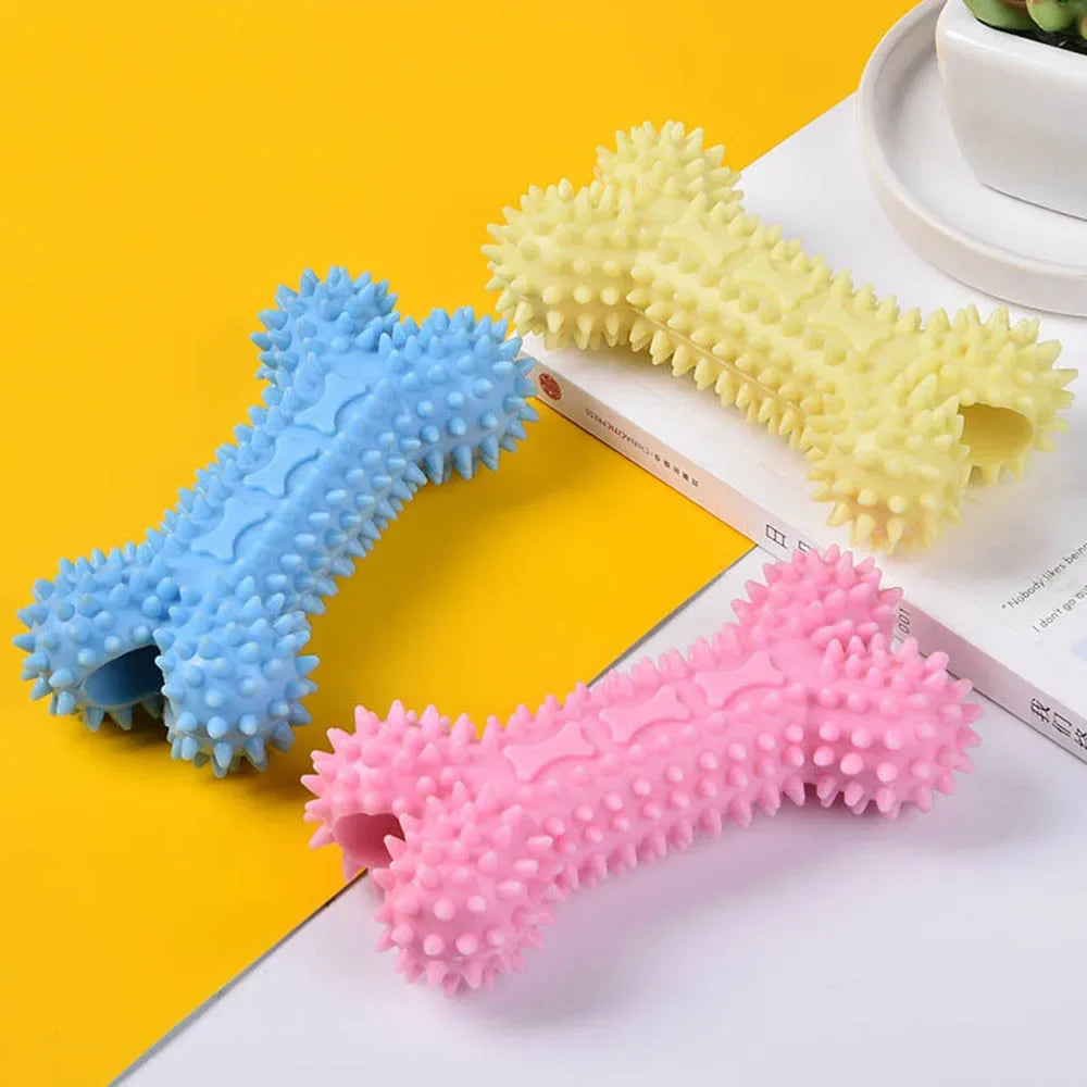 Three spiked rubber dog bone toys in blue, yellow, and pink on a yellow background