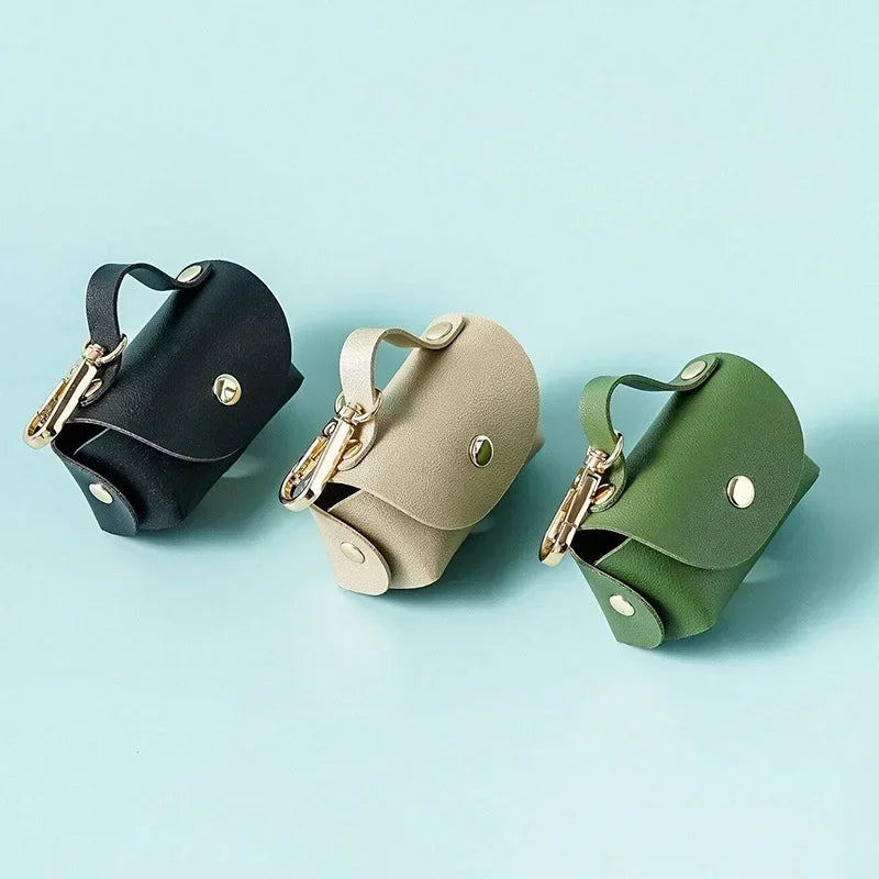 Black, beige, and green leather dog waste bag holders with gold clips on light blue background