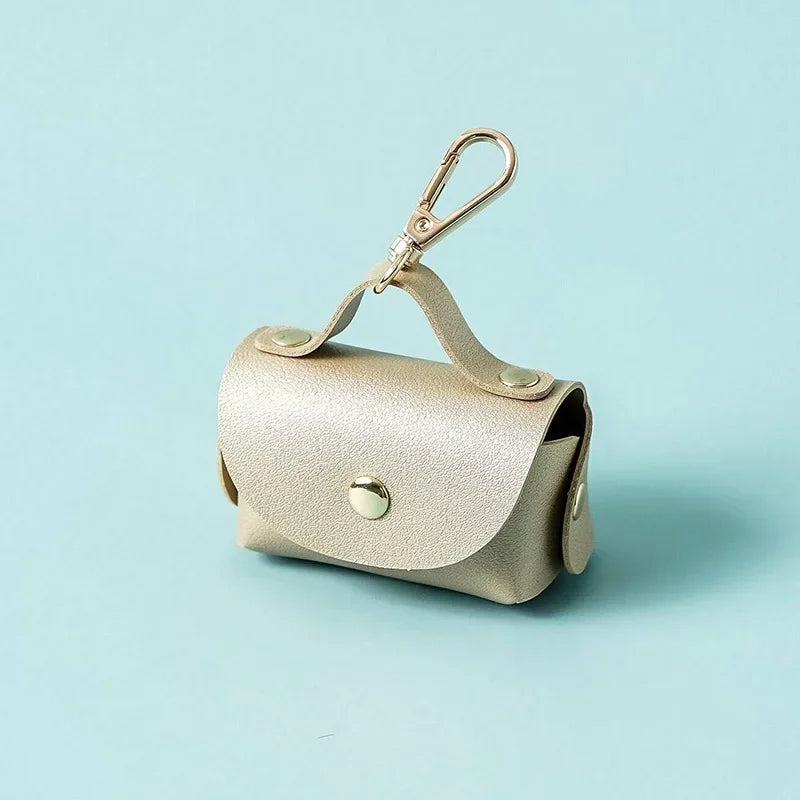 Gold dog waste bag holder with metal clip on a light blue background