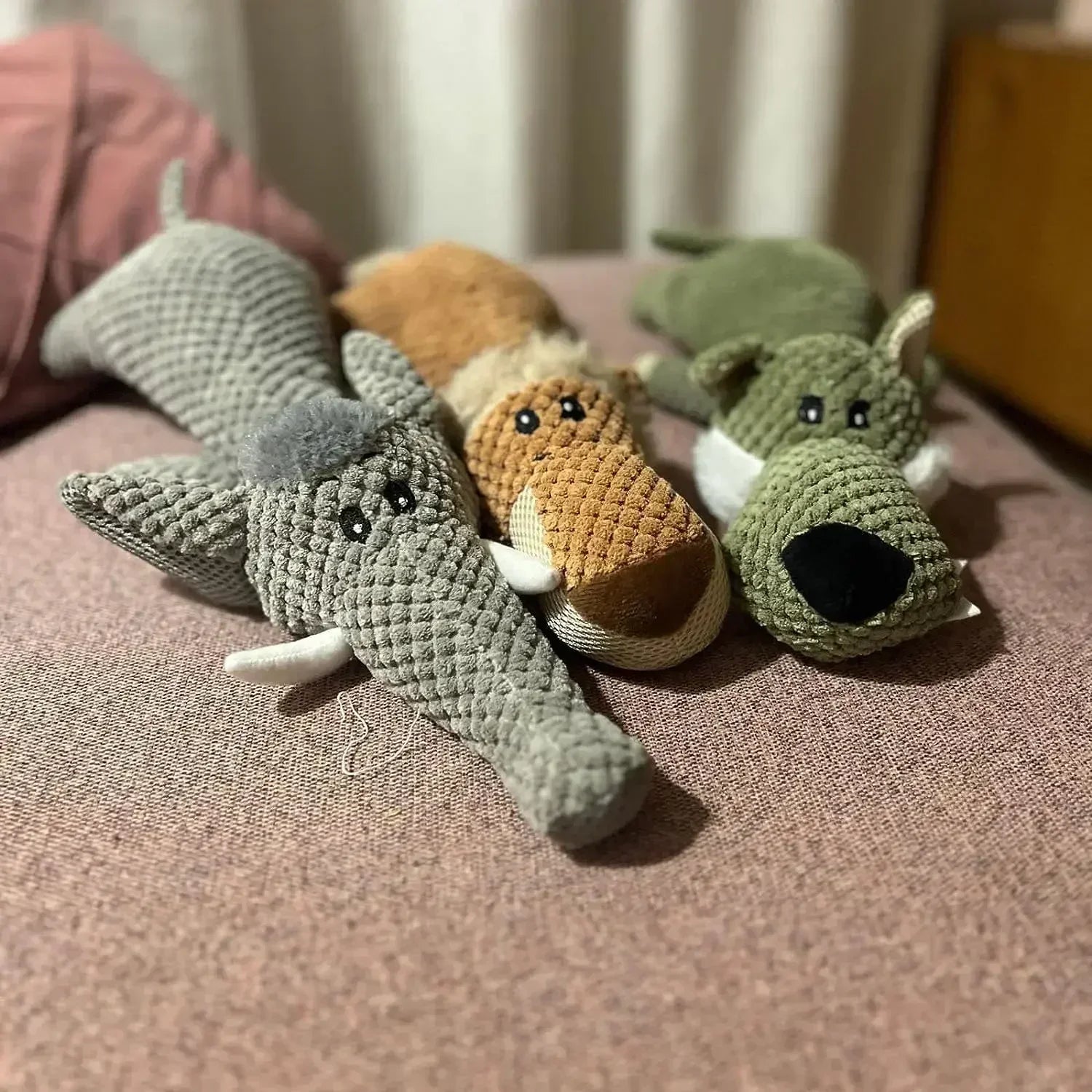 Plush animal dog toys in crocodile, fox, and wolf designs on a pink fabric surface