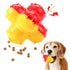 Dog chewing red and yellow interactive treat-dispensing toy with kibble, white background