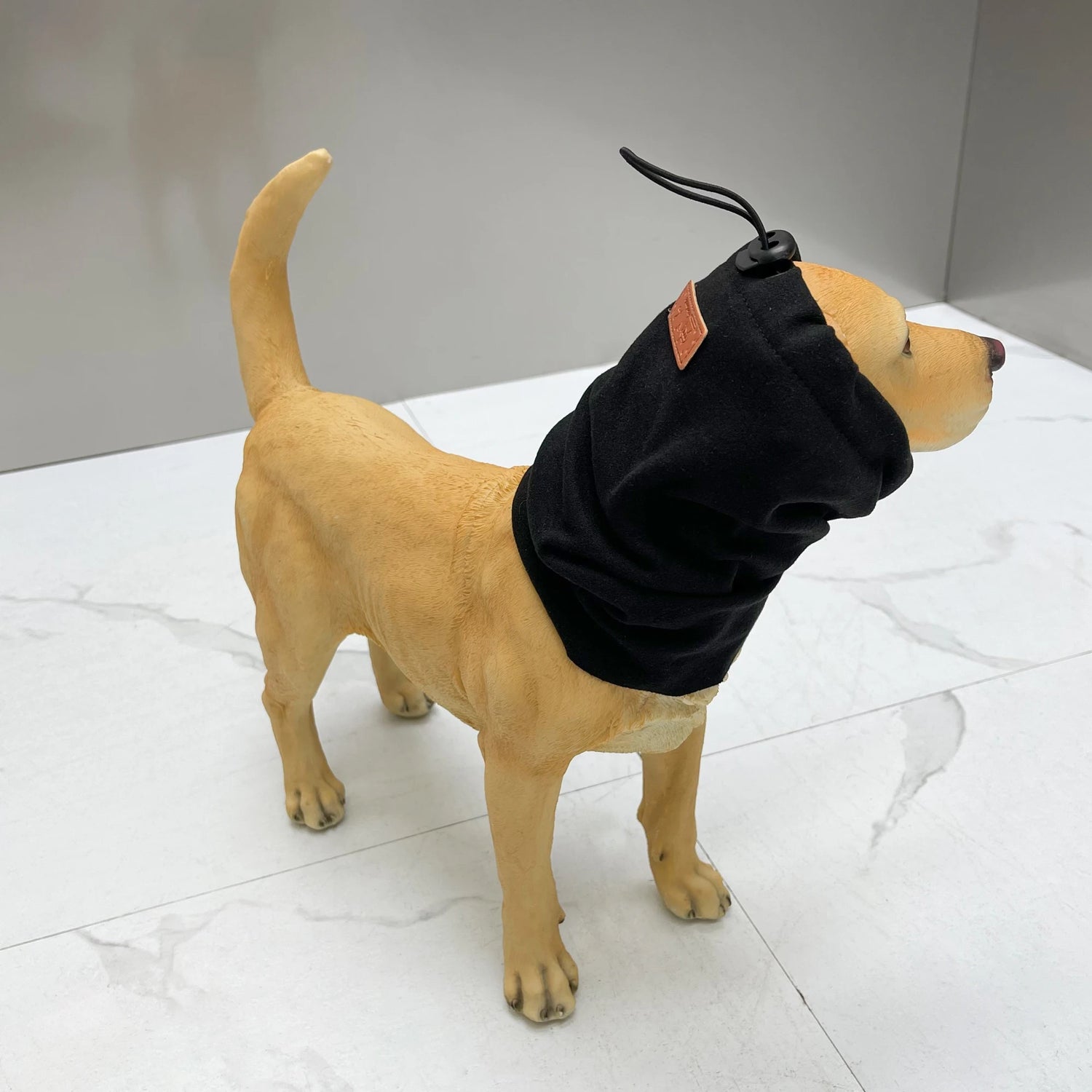 Dog mannequin wearing black fleece dog snood with adjustable toggle on neck, indoor setting