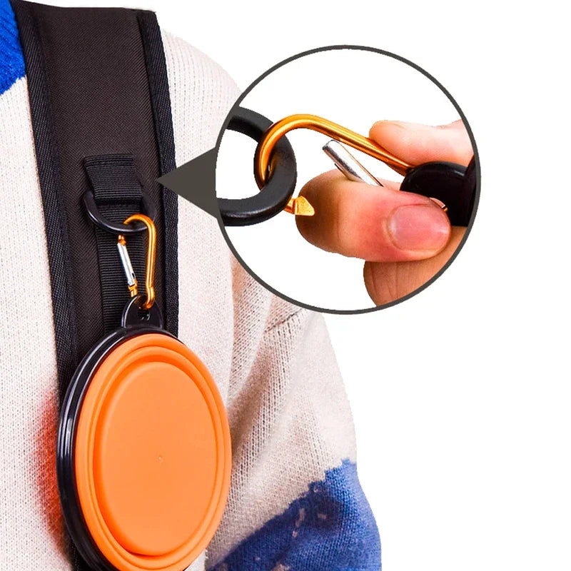 Orange collapsible pet travel bowl clipped to backpack with carabiner for portable dog and cat food and water on outdoor trips