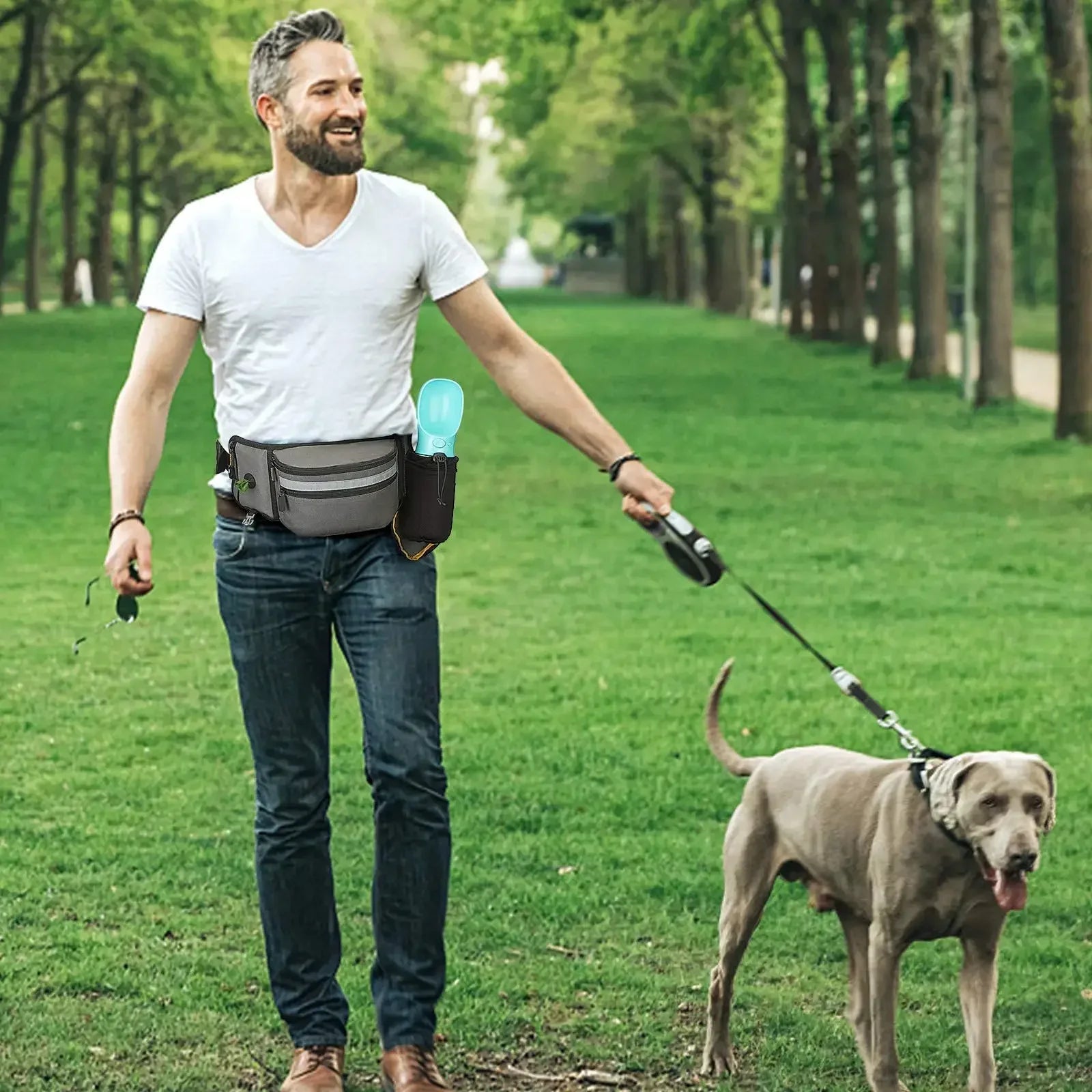 Man walking dog in park wearing dog walking waist bag with water bottle and accessories