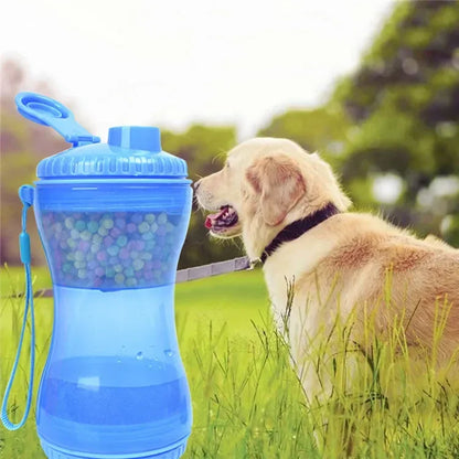 Dog outdoors beside blue portable pet water and treat bottle in grassy field