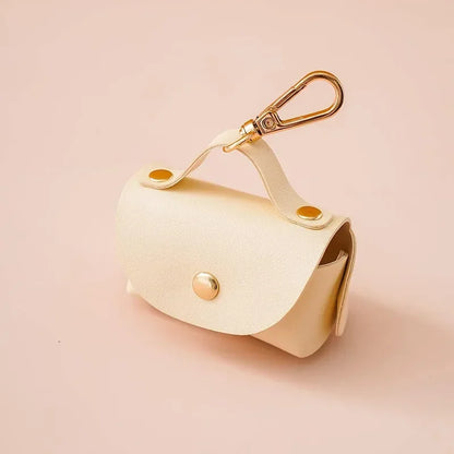 Cream dog waste bag holder with gold clasp and snap button, pet accessory on beige background
