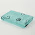 Folded turquoise dog towel with black paw and bone prints on white background