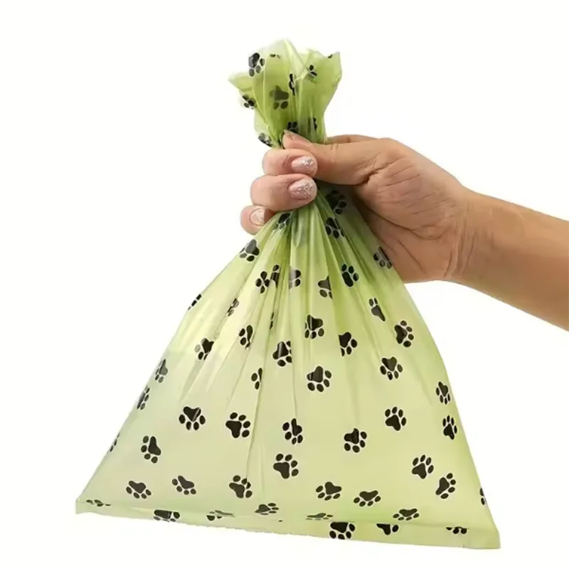 Hand holding green dog waste bag with black paw prints, pet cleanup accessory