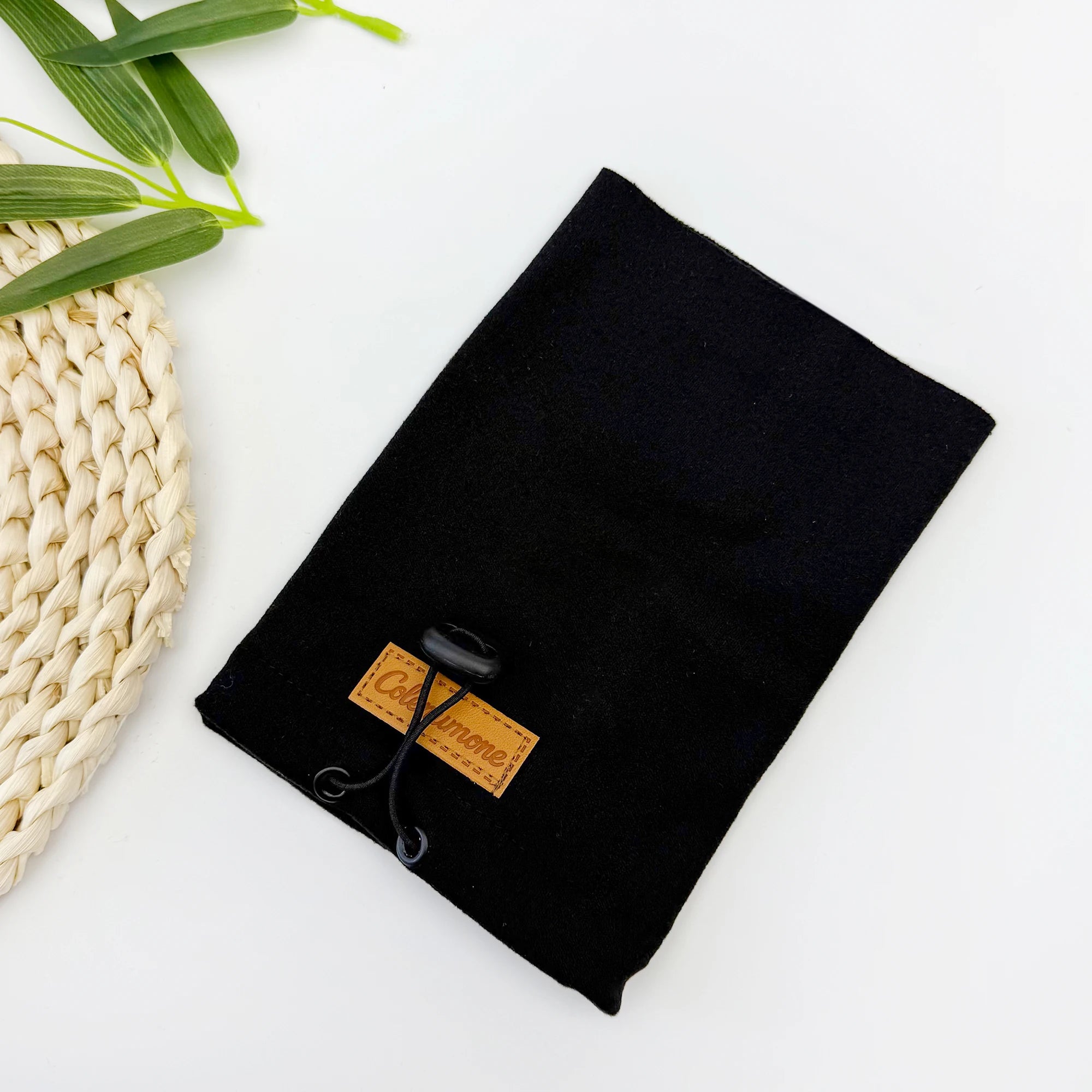 Black drawstring pouch for dog accessories on white background with woven mat and leaves
