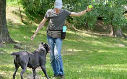 Man with dog training pouch and water bottle playing fetch with black dog in park