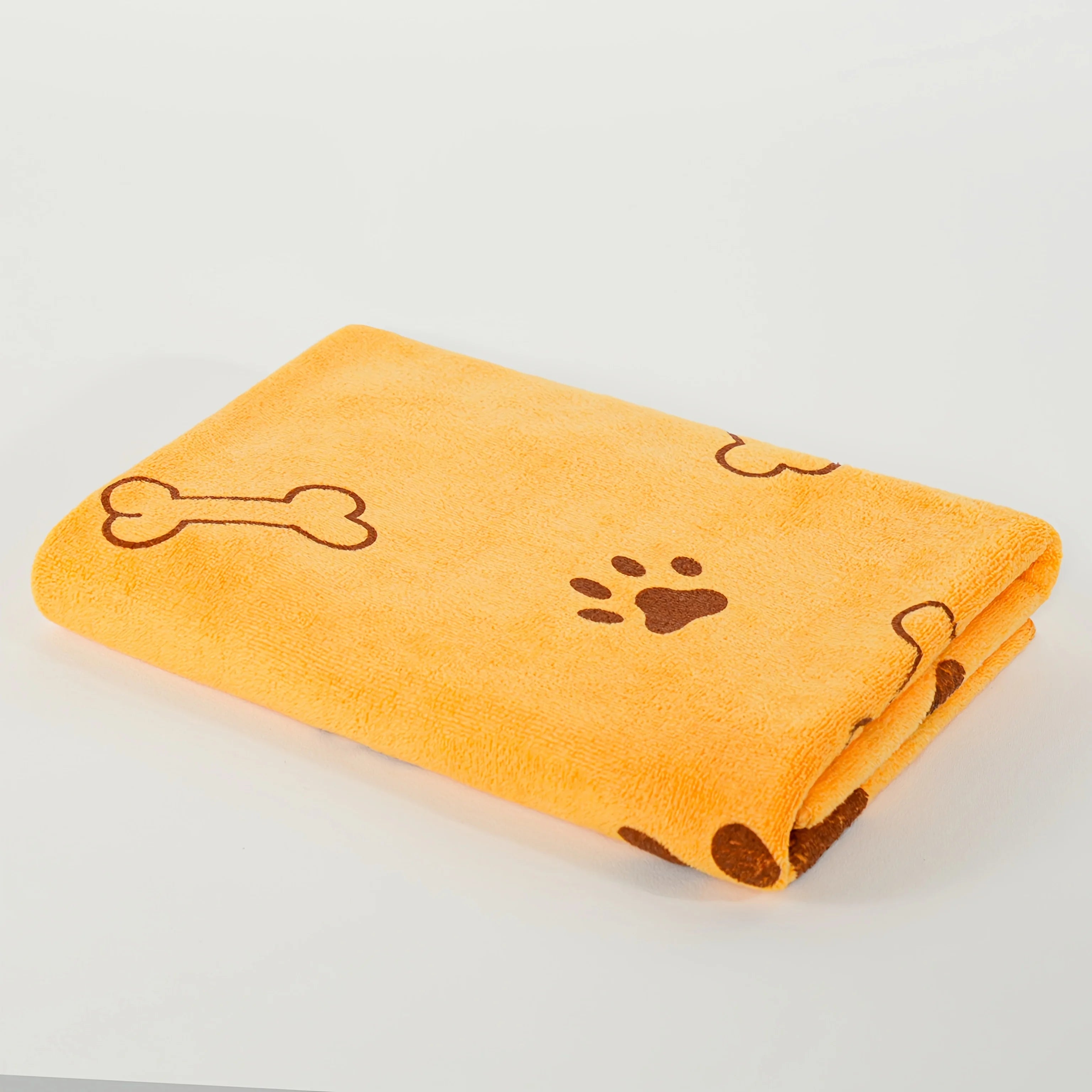 Folded yellow dog towel with brown paw prints and bone patterns on white background