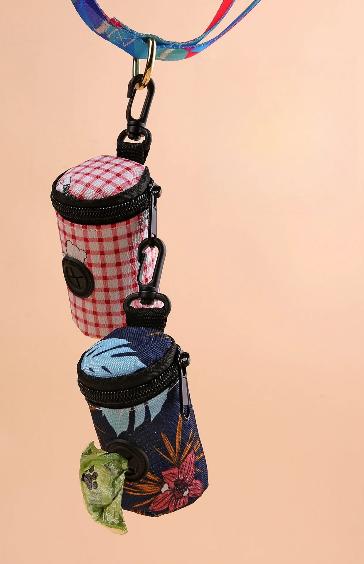 Two colorful dog waste bag holders attached to a leash, floral and gingham patterns