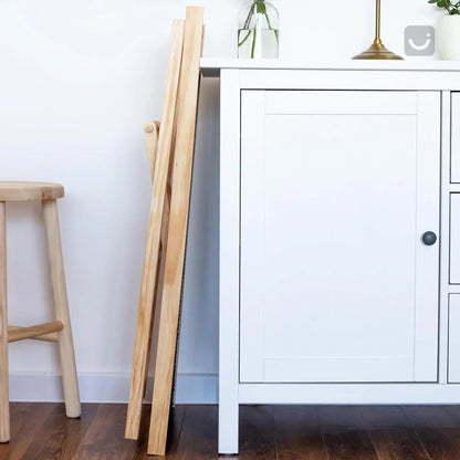 Adjustable wooden dog ladder folded beside a white cabinet, showcasing its lightweight and space-saving design.