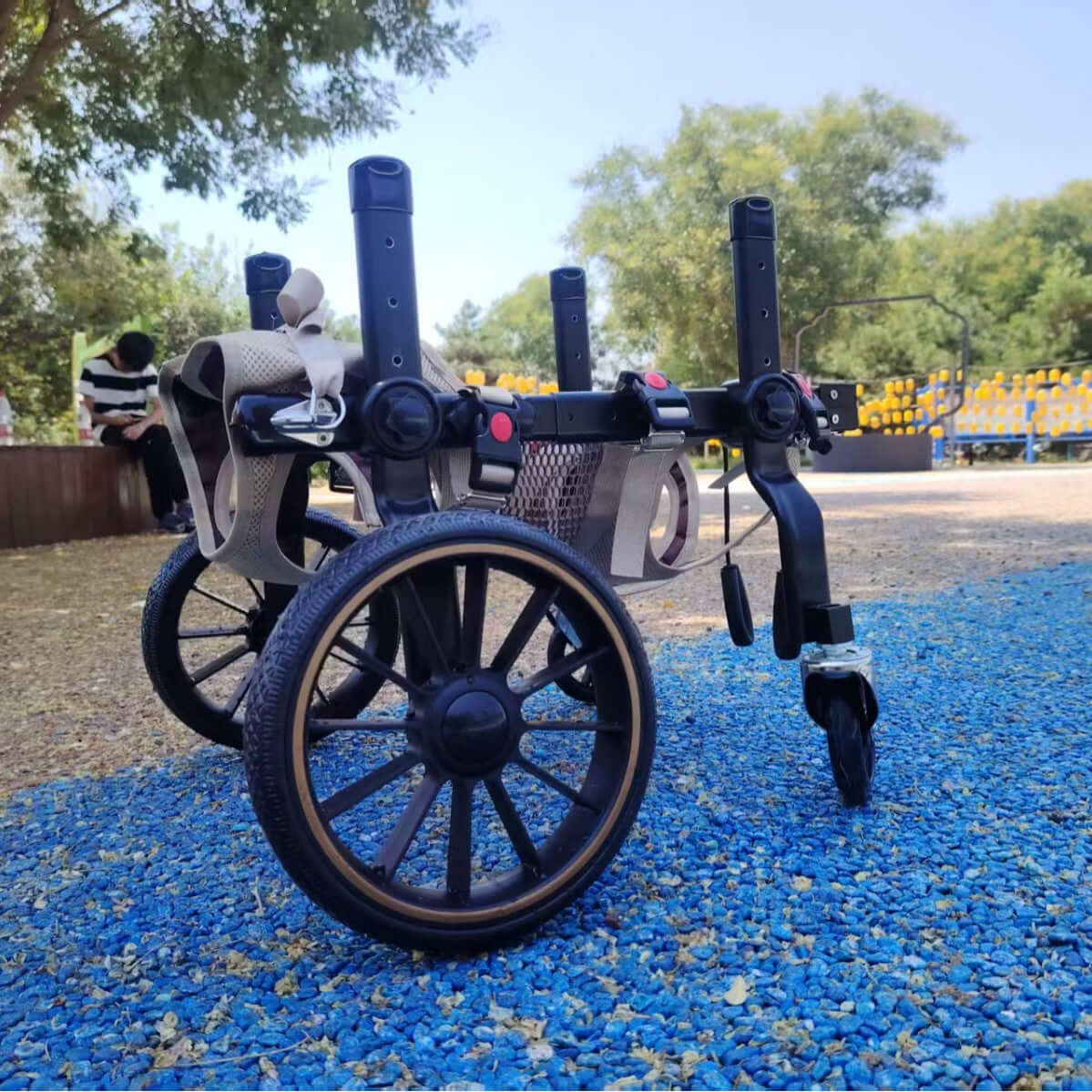 Dog wheelchair for hind limb paralysis placed on blue gravel in a park, designed for mobility aid for disabled dogs.