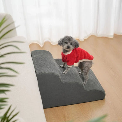 A small dog in a red sweater standing on non slip dog stairs for small dogs next to a sofa.