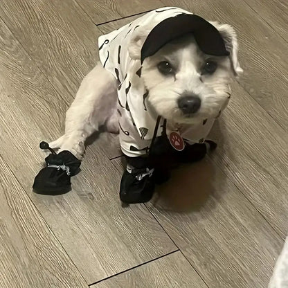 Small dog wearing waterproof dog boots and a hooded outfit, standing on a wooden floor indoors